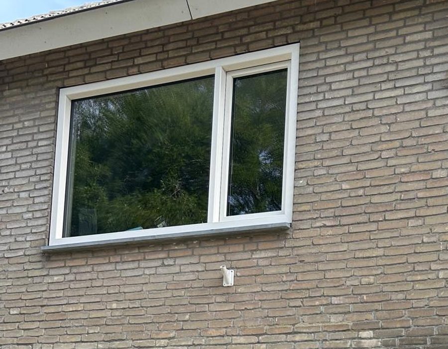 Nieuw wit kunststof raam met vast deel en draaikiepdeel in een bakstenen gevel