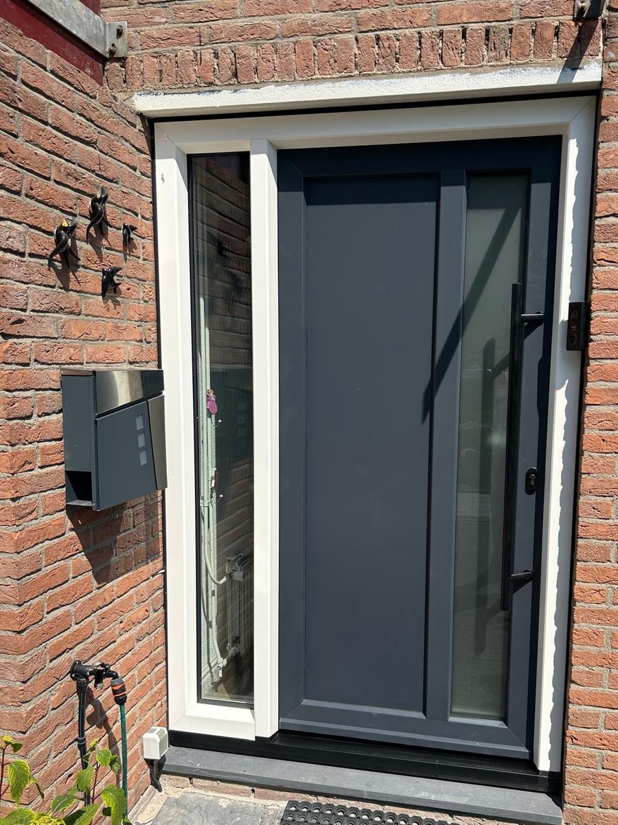Antraciete kunststof voordeur met zijlichten en zwarte greep in een gemetselde gevel